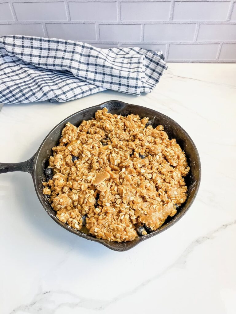 Blueberry peach crisp with a buttery topping in a cast iron skillet ready to bake.