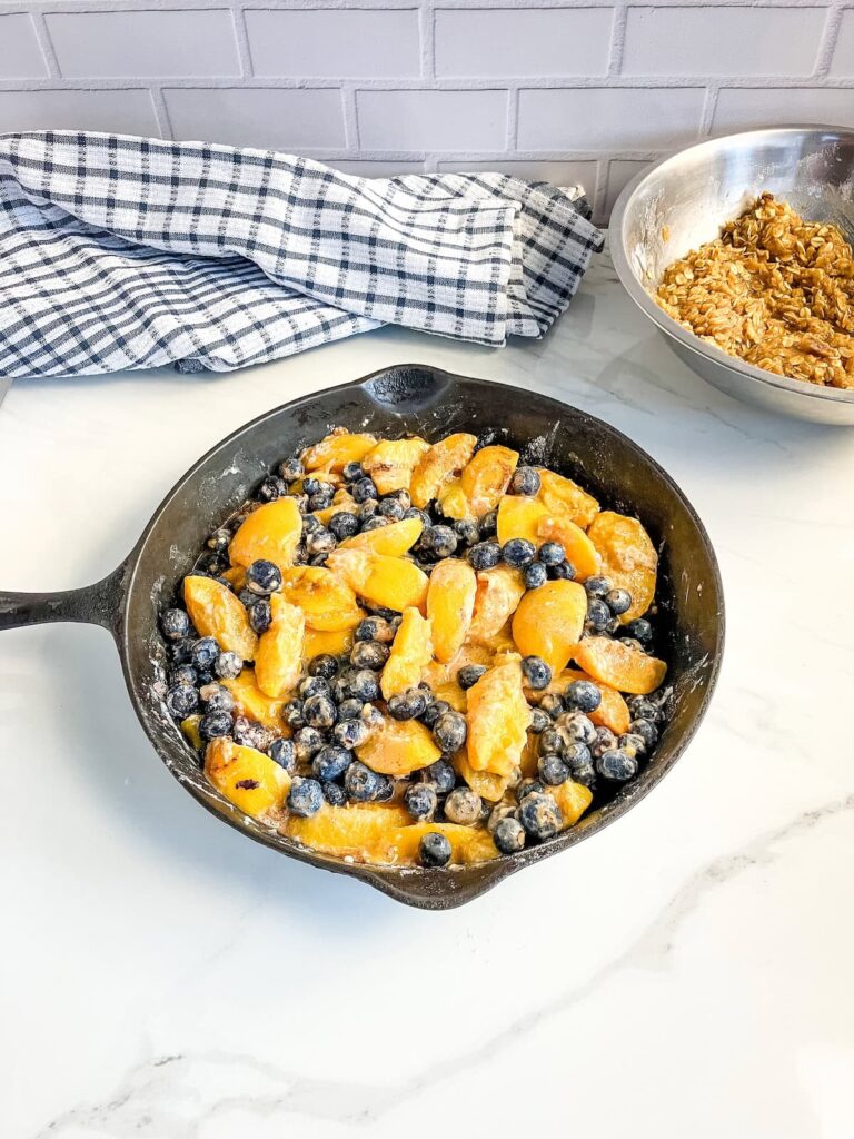 Peaches and blueberries mixed with sugar and flour to make a filling in a cast iron skillet.