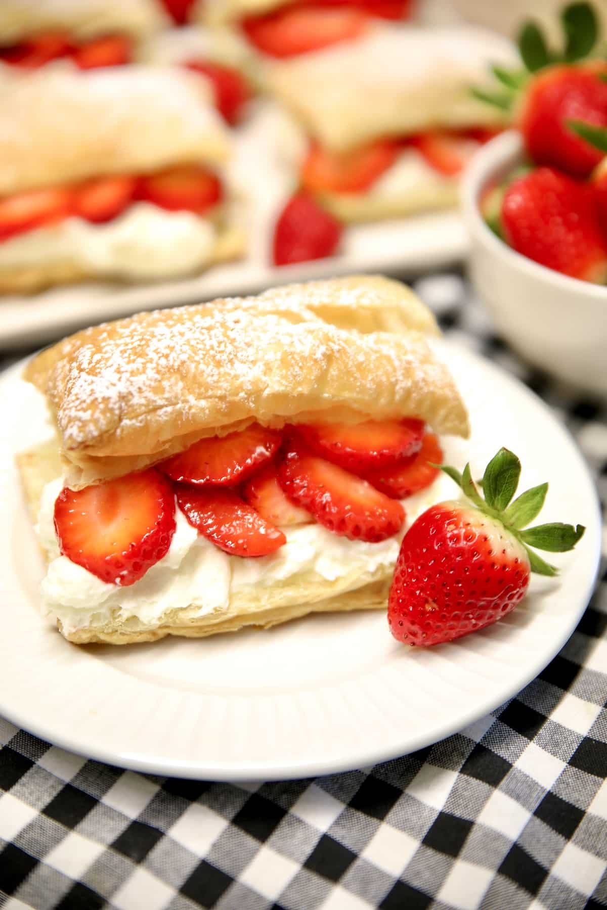 Homemade strawberry napoleons on white plates, puffed pastry filled with layers of strawberries and whipped cream.