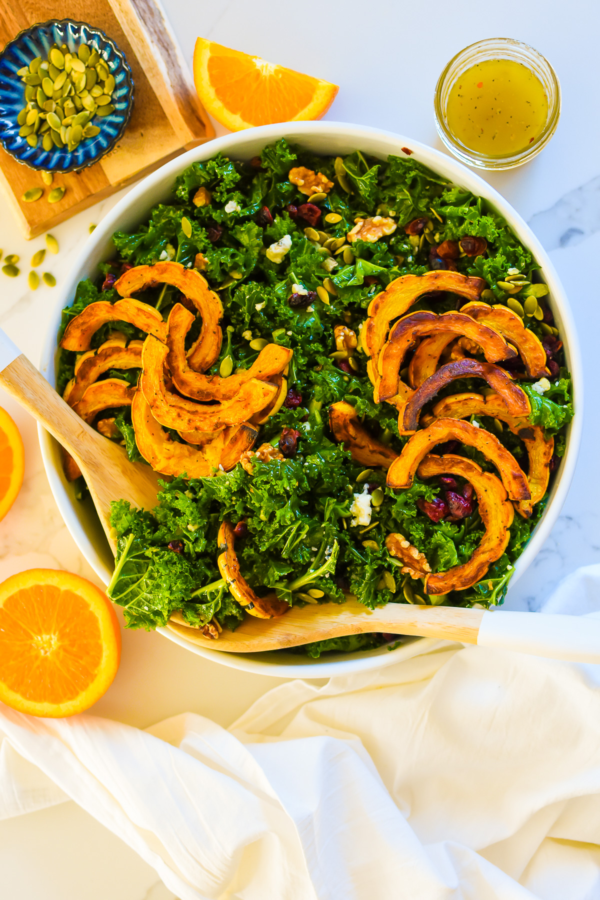 A large salad bowl filled with a kale salad and roasted delicata squash.