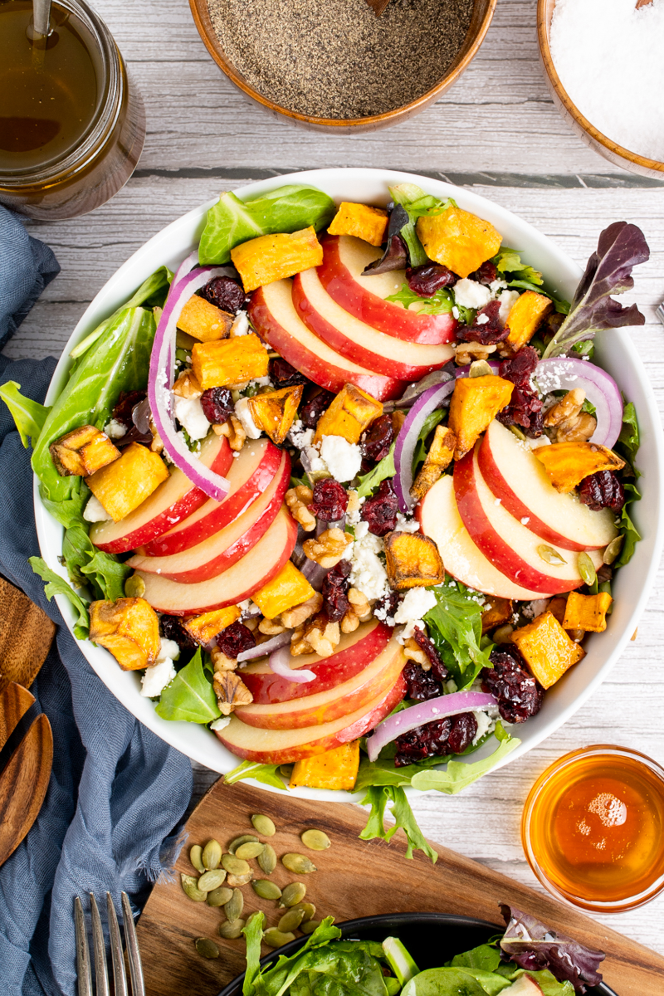 A white salad bowl filled with fresh greens, vegetables, and apples.