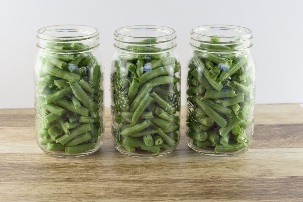 3 quart mason jars filled with cut green beans and sitting on a wooden table.