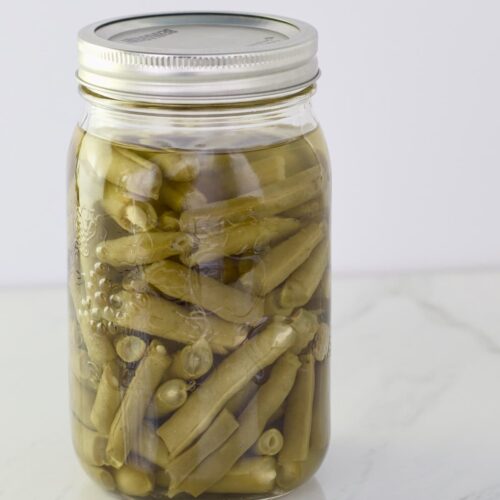A quart jar of home canned green beans sitting on a counter.