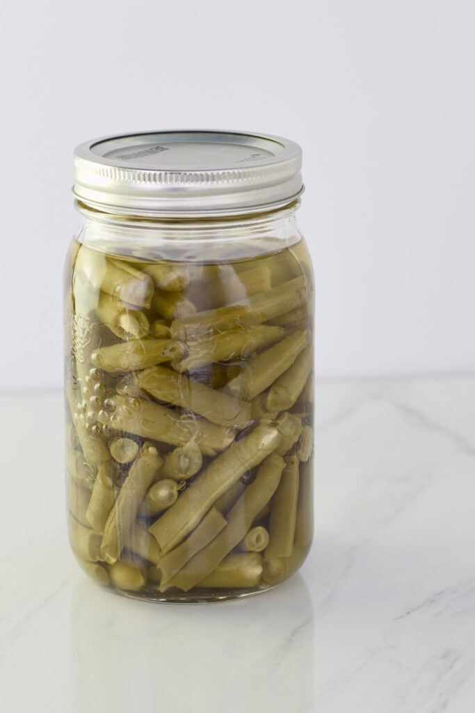 A quart jar of home canned green beans sitting on a counter.