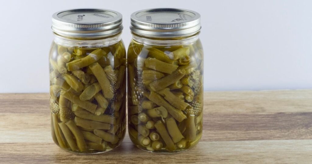 Two quart jars of canned green beans on a wooden table.