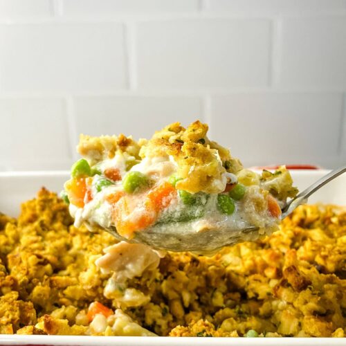 Homemade leftover turkey and stuffing casserole with a serving spoon lifting a serving out of the casserole dish.