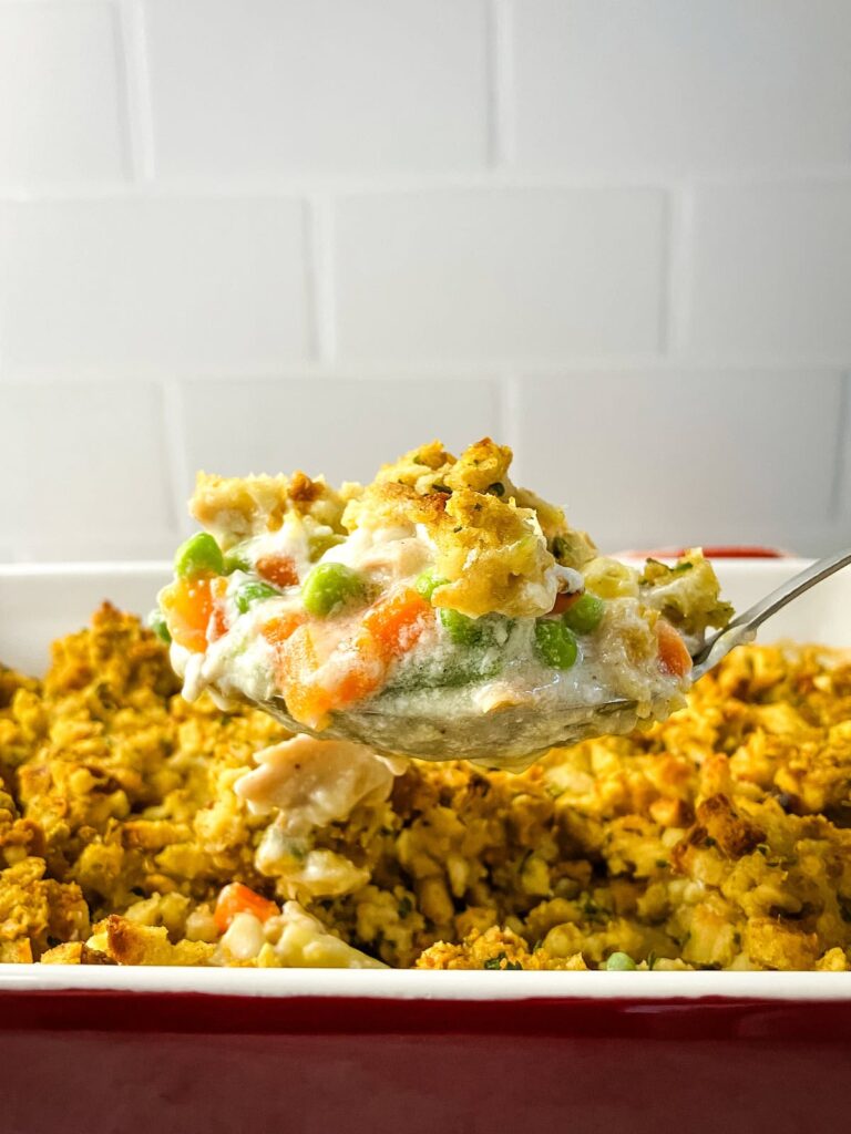 Homemade leftover turkey and stuffing casserole with a serving spoon lifting a serving out of the casserole dish.