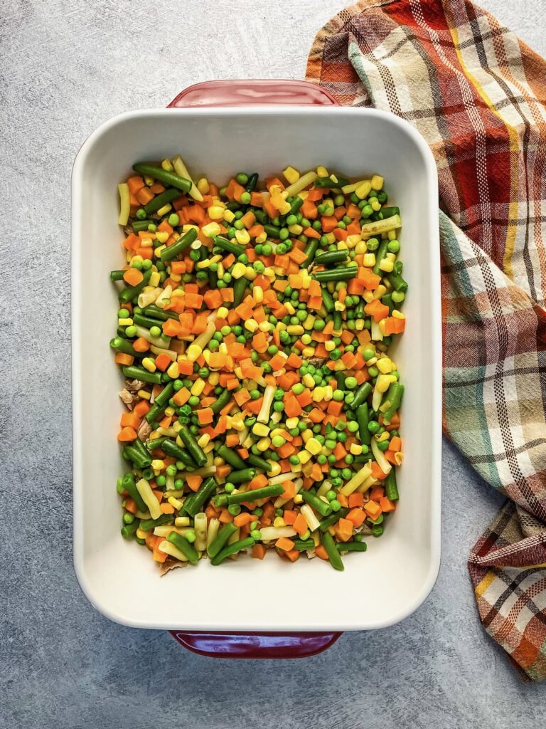 Layer of frozen vegetables over top of the cooked turkey in a casserole dish.