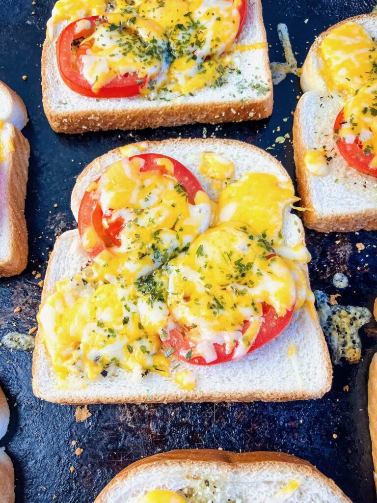 Cheesy garlic toast with tomatoes on a baking sheet.