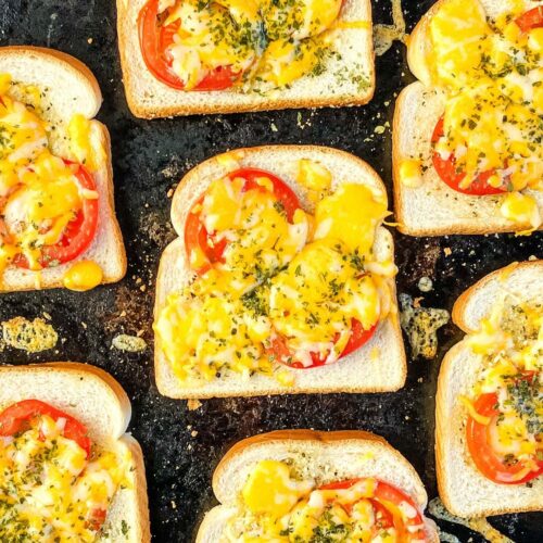 Cheesy garlic toast with tomatoes on a baking sheet.