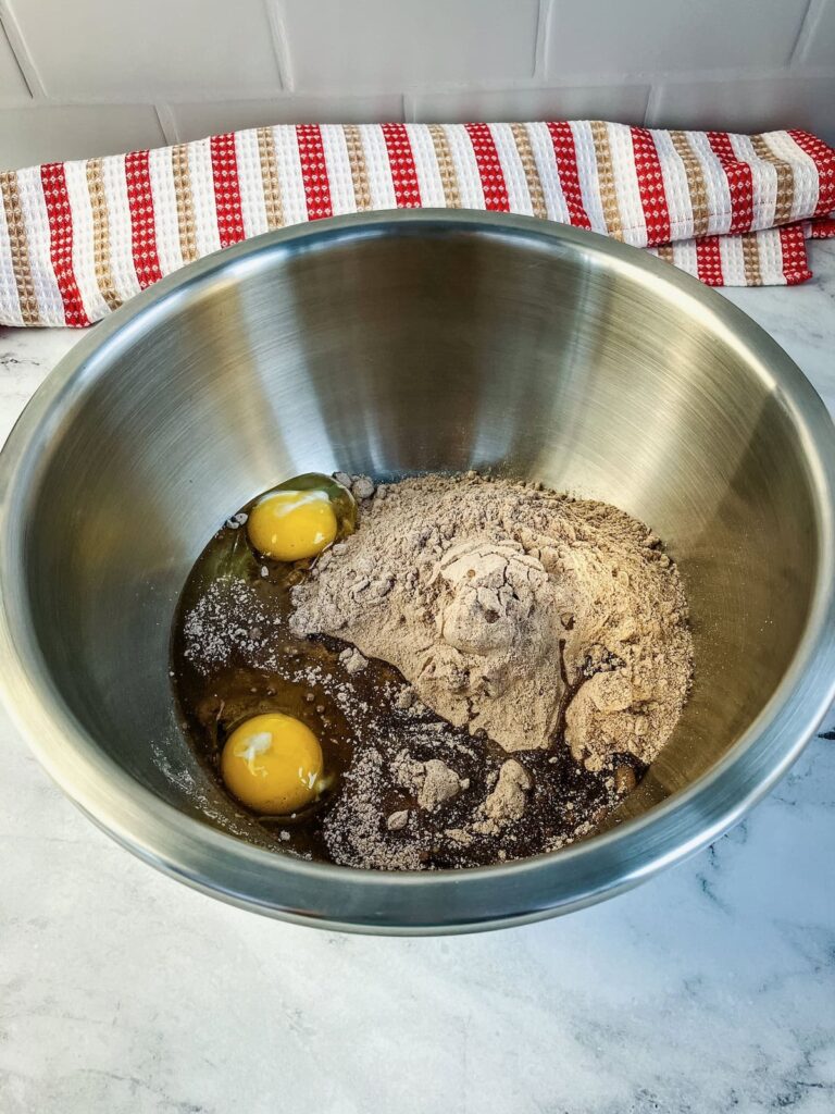 A mixing bowl filled with a chocolate fudge cake mix, eggs, and vegetable oil.
