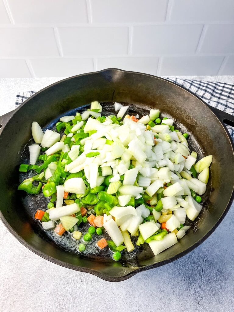 Cooking carrots, corn, peas, onions, and peppers in a skillet.