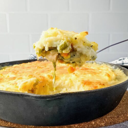 Lifting a serving spoon of leftover turkey shepherd's pie out of a cast iron skillet.
