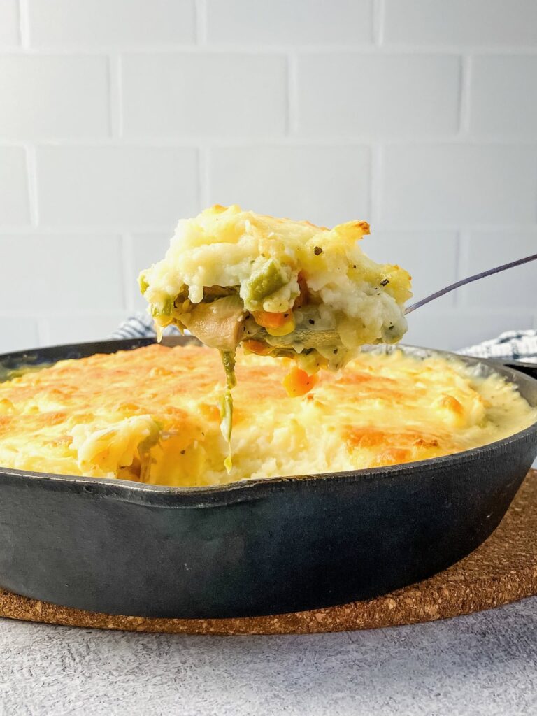 Lifting a serving spoon of leftover turkey shepherd's pie out of a cast iron skillet.