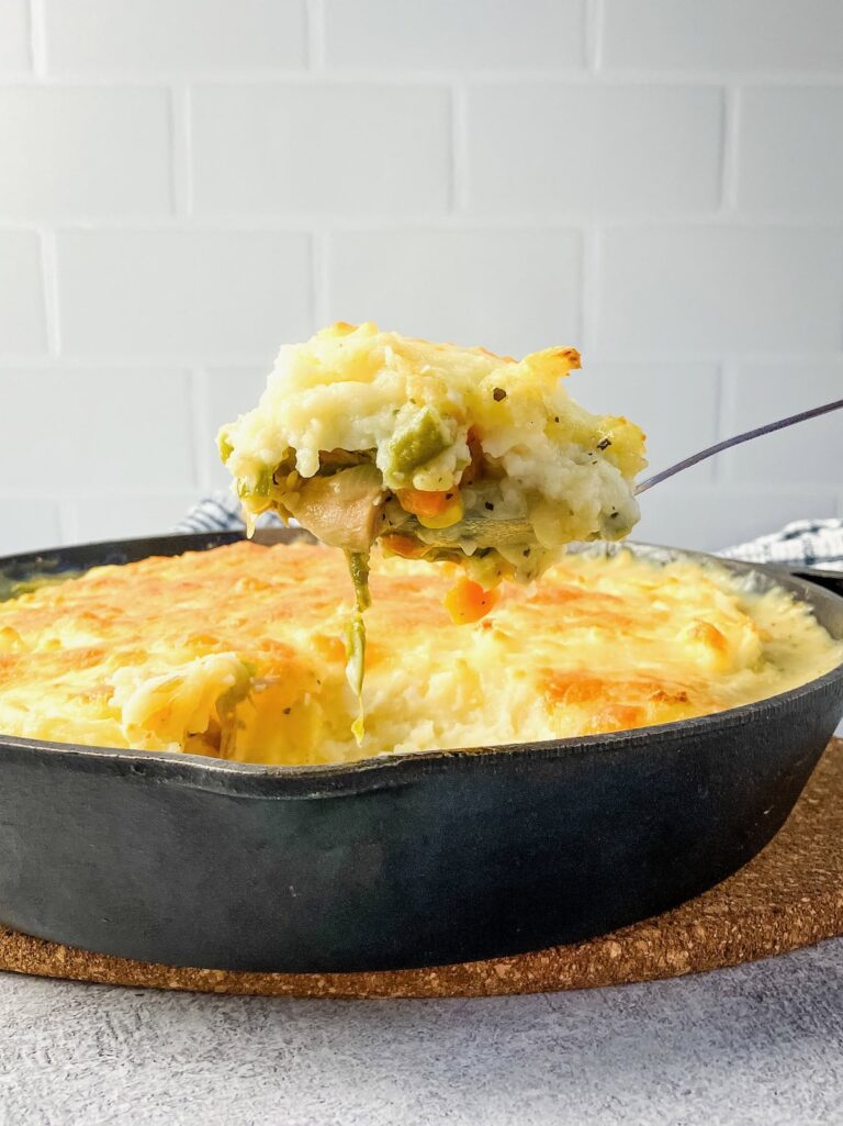 Lifting a serving spoon of leftover turkey shepherd's pie out of a cast iron skillet.