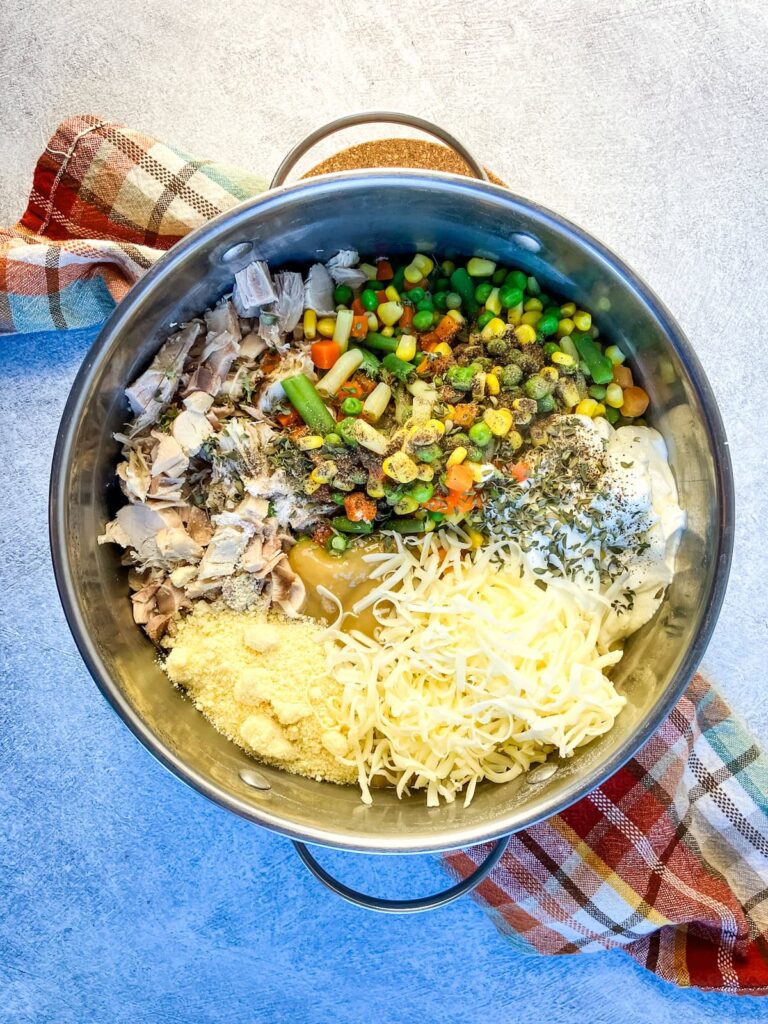 Cooked egg noodles with mixed vegetables, cooked turkey, sour cream, cheese and seasonings in a pot.