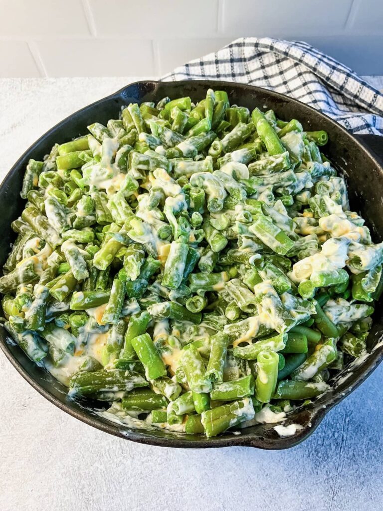 Adding cooked green beans to the sauce mixture.