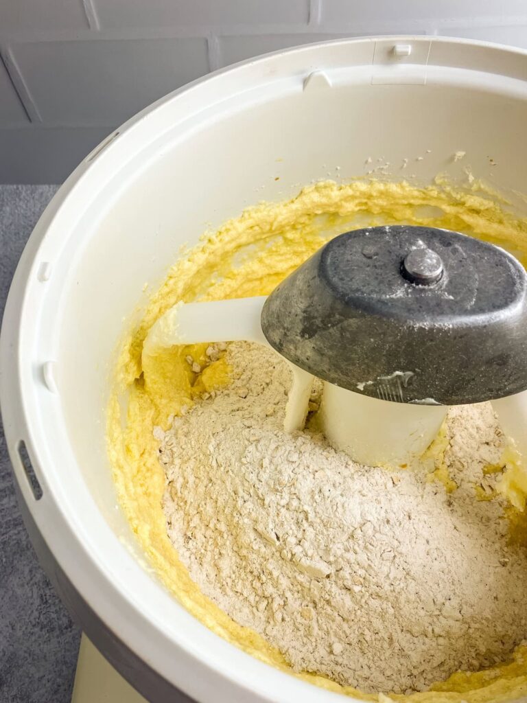 Flour mixture added to wet ingredients in the bowl of a stand mixer.