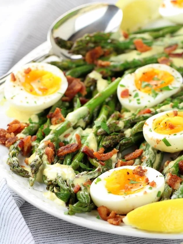 Asparagus, egg and bacon salad on a white serving tray.