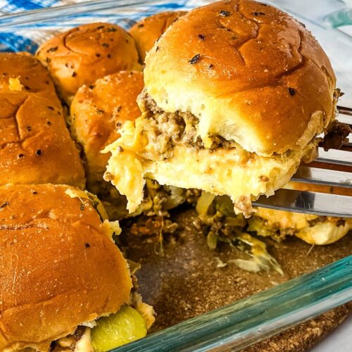 Homemade cheeseburger sliders in a baking dish with one being lifted out of the pan.