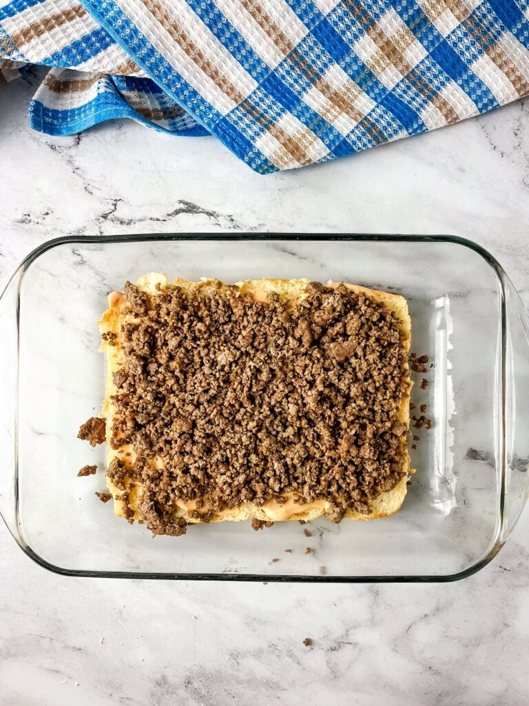 Cooked ground beef placed on top of the cheese sauce on the rolls.