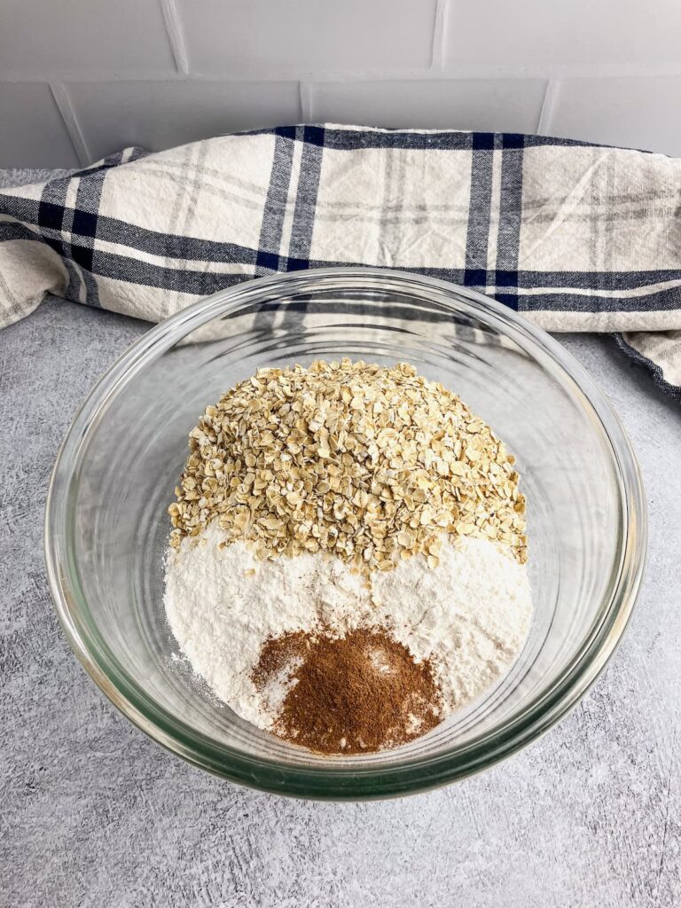 A medium sized glass mixing bowl with flour, oatmeal, and other dry ingredients.