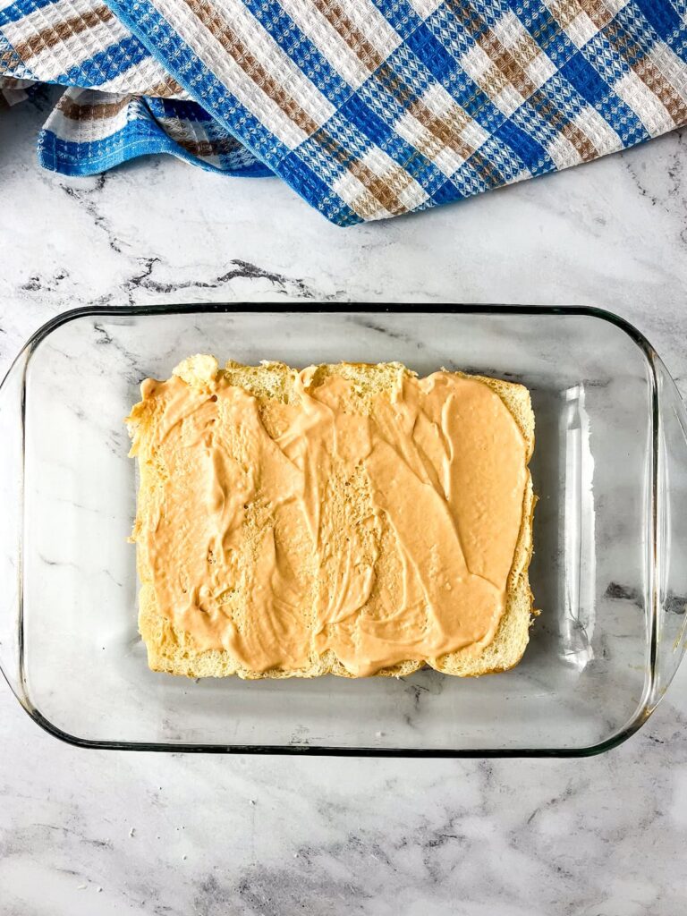 Hawaiian rolls cut in half sitting in a baking dish and spread with homemade burger sauce.