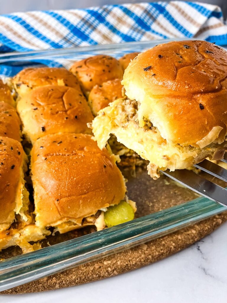 Lifting a cheeseburger slider out of a baking dish with a spatula.