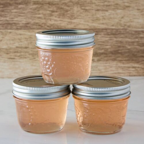 Three jars of homemade red clover jelly in small jelly jars with one stacked on top of the other two jars.