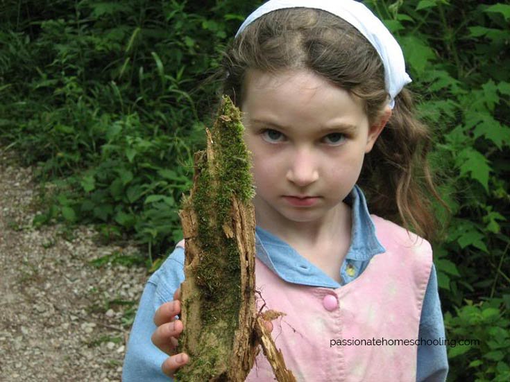 Girl holding part of a fallen log covered in green moss.