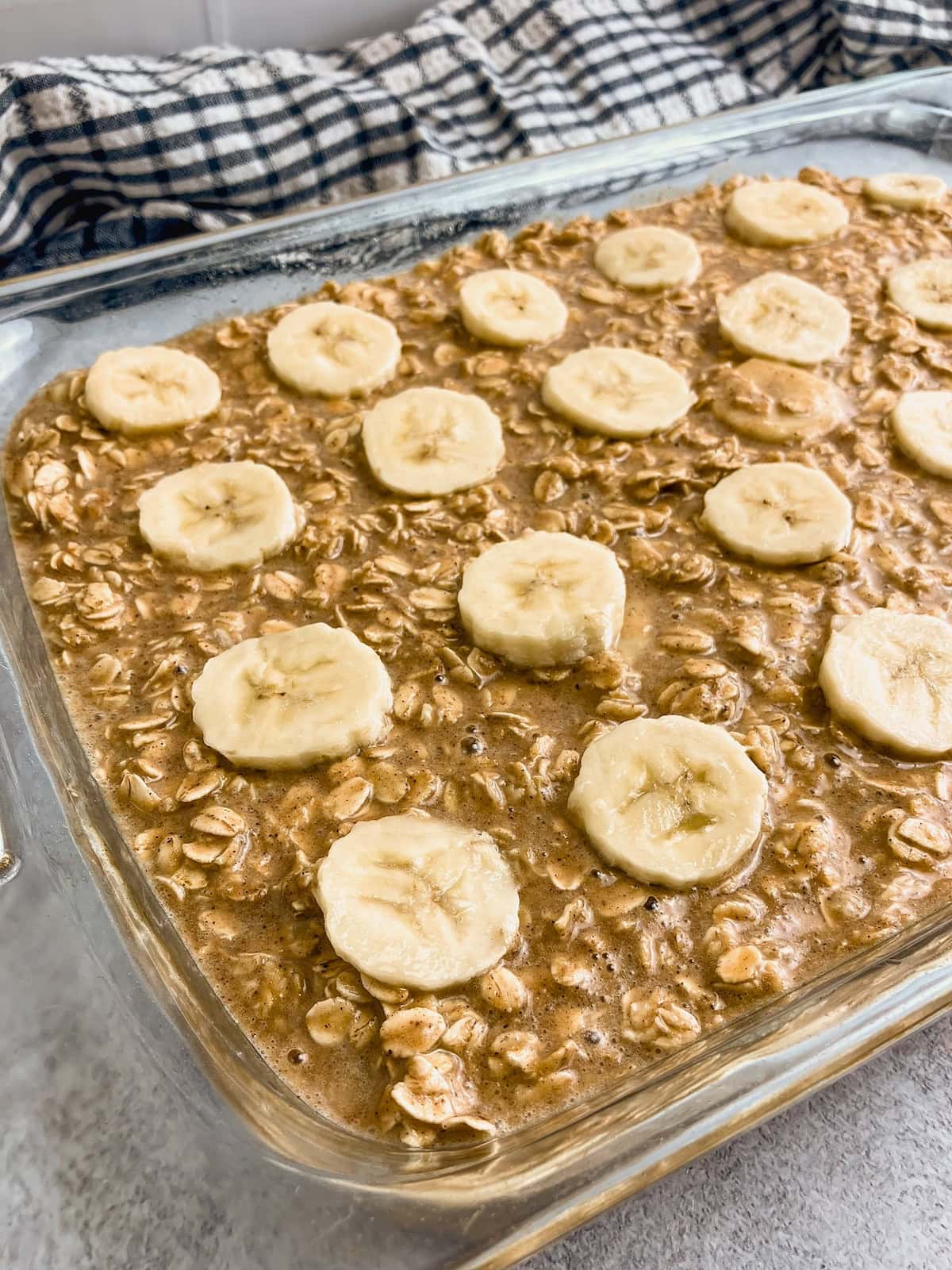 Peanut butter banana baked oatmeal batter in a baking dish and topped with slices of banana.
