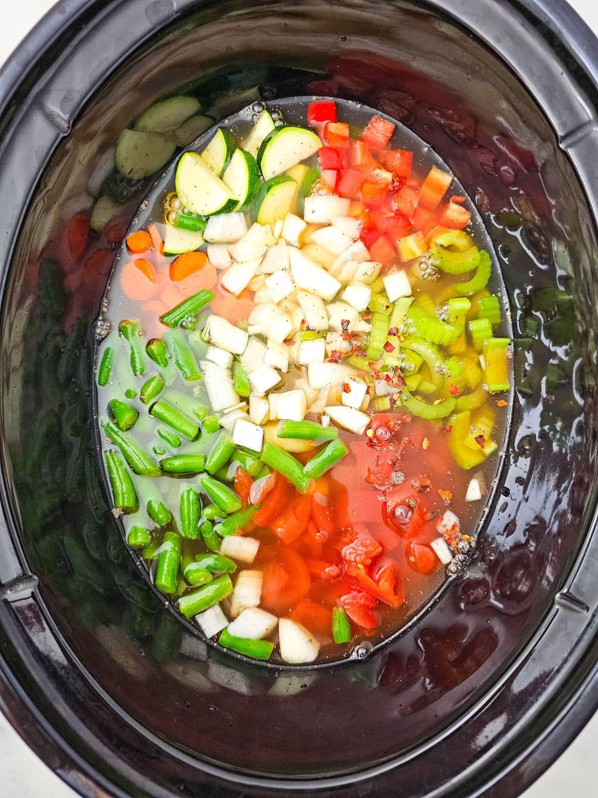 Vegetable broth poured over the chopped vegetables and seasoning in the slow cooker.