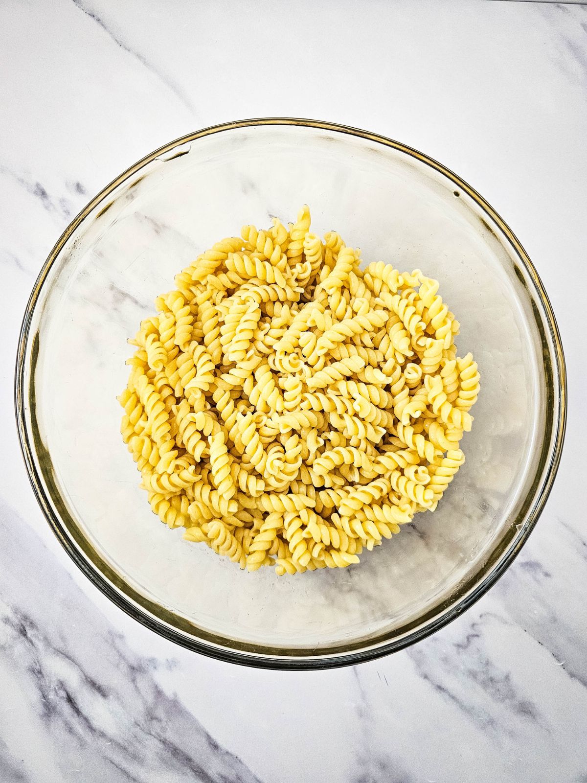 A bowl of cooked rotini pasta on a marble counter.
