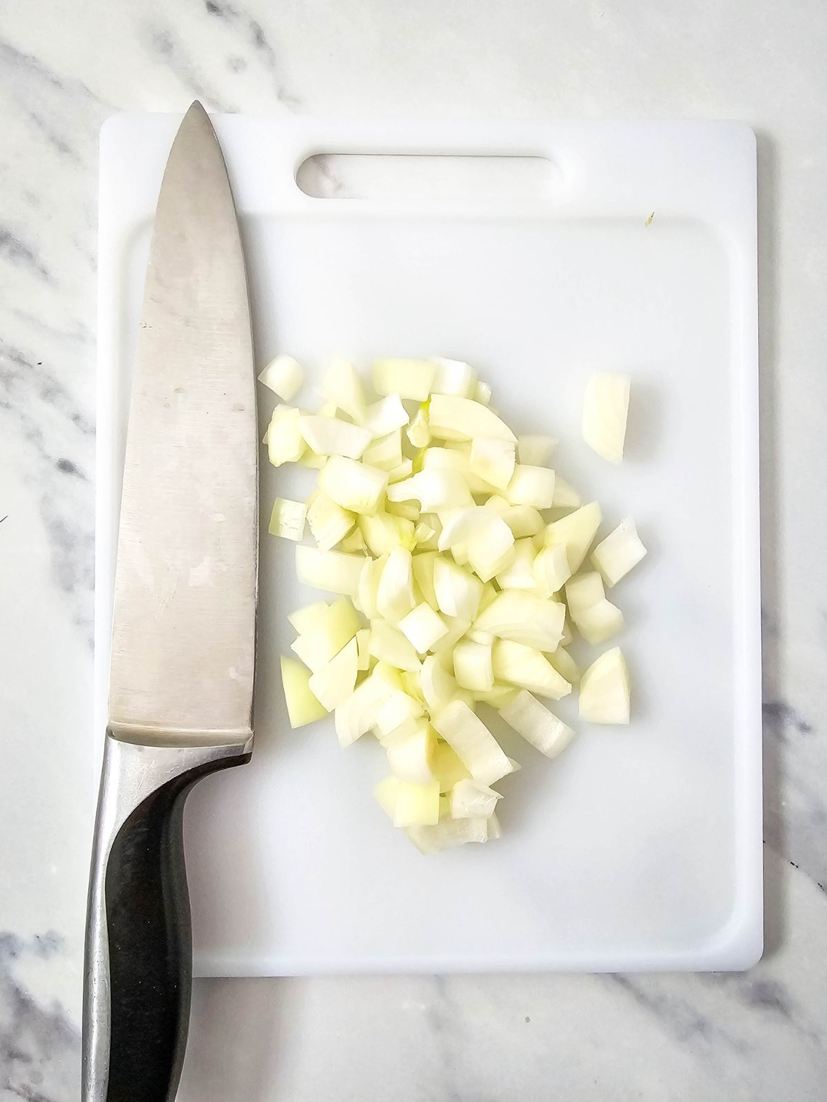 A cutting board with a knife and a diced onion.