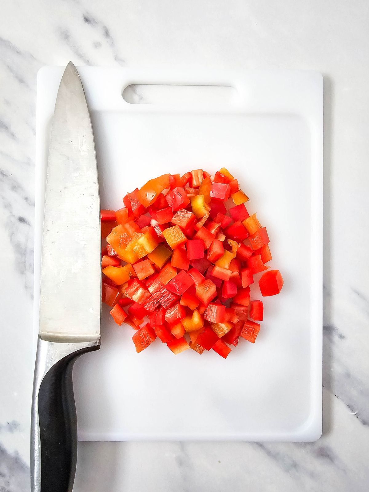 Diced red bell pepper on a cutting board with a knife.