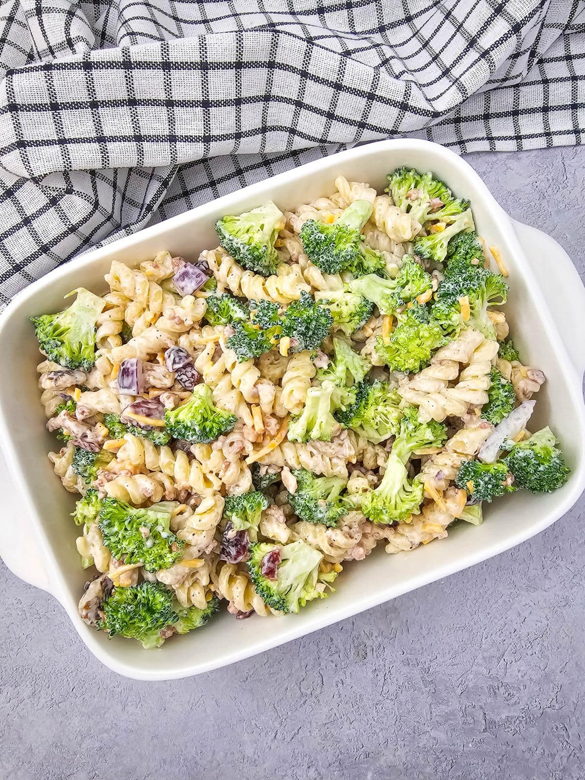 Broccoli pasta salad with cheese and bacon in a white serving dish.