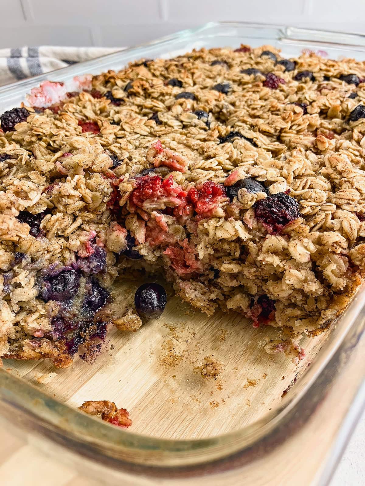 A glass 9x13 inch baking dish of mixed berry baked oatmeal with a slice removed.
