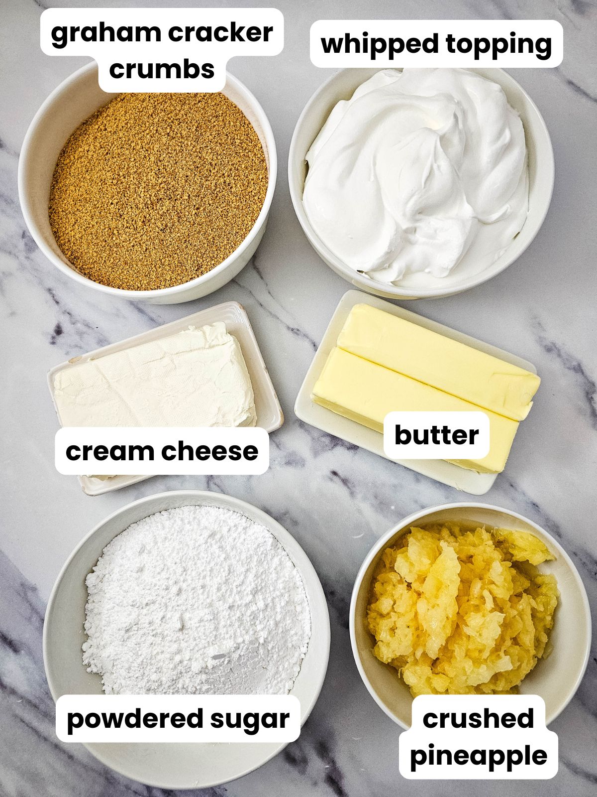 Ingredients to make pineapple dream dessert in bowls including graham cracker crumbs, whipped topping, cream cheese, butter, powdered sugar, and crushed pineapple.