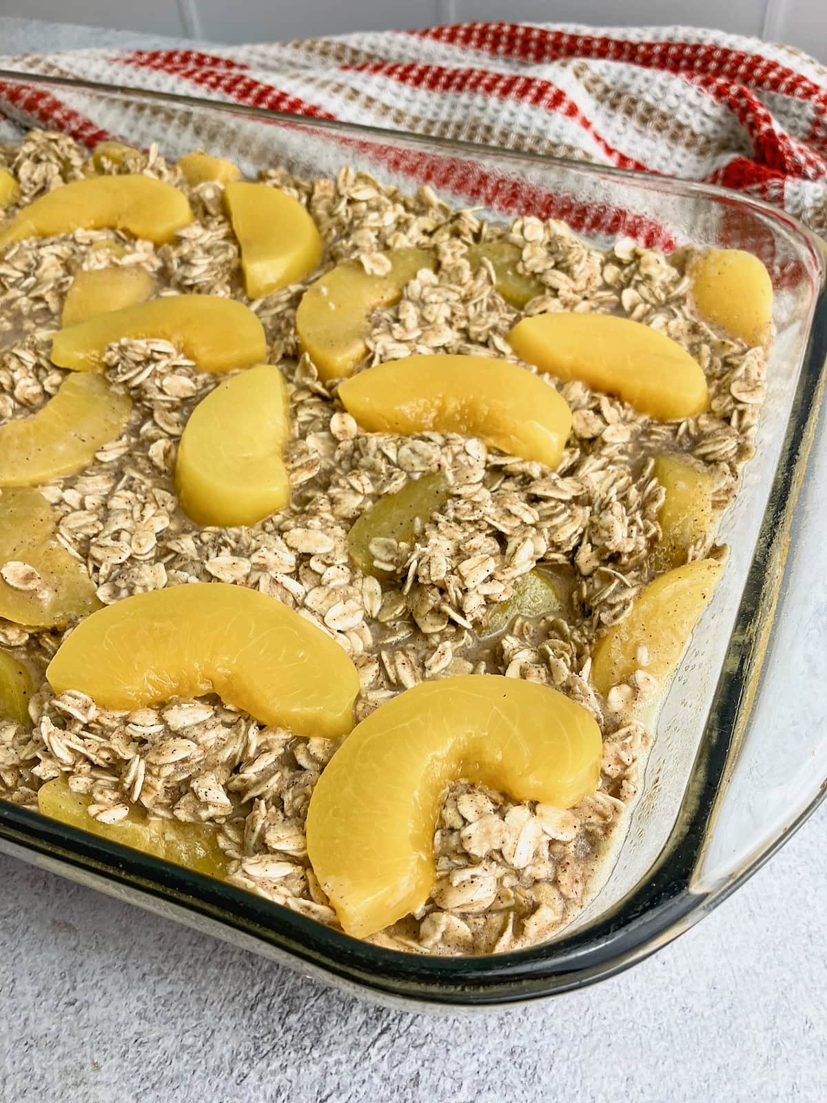 A glass baking dish of peach baked oatmeal batter with sliced peaches spread over the top.