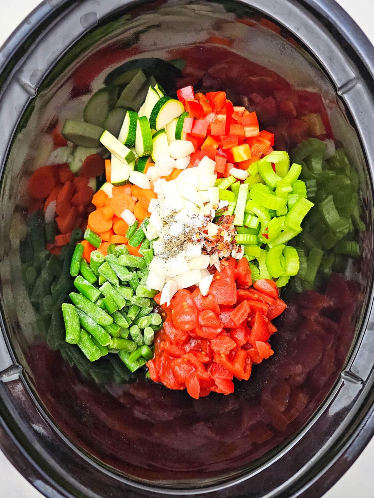 Salt, pepper, and chili flakes were added to the vegetables in the slow cooker.