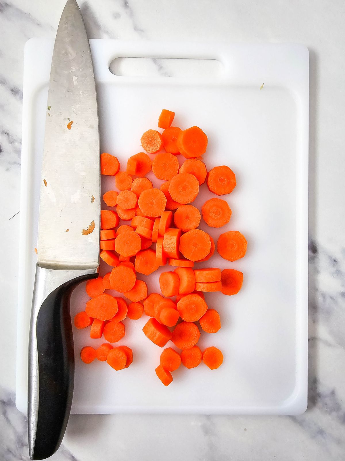 A knife on a cutting board with sliced carrots.