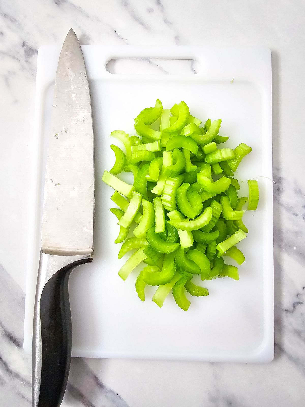 A knife and a cutting board with chopped celery.