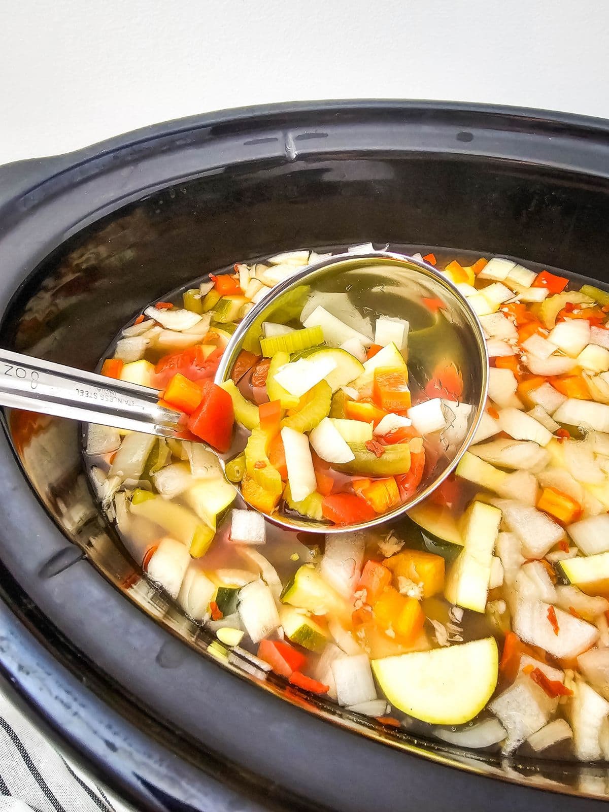Ladling homemade vegetable soup out of a slow cooker.