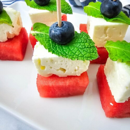 Watermelon, feta cheese, and blueberry skewers on a platter.