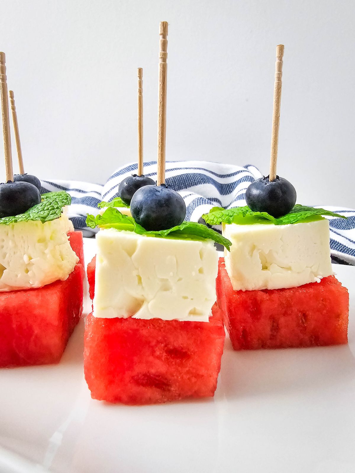 A platter filled with watermelon, feta cheese, and blueberry skewers.
