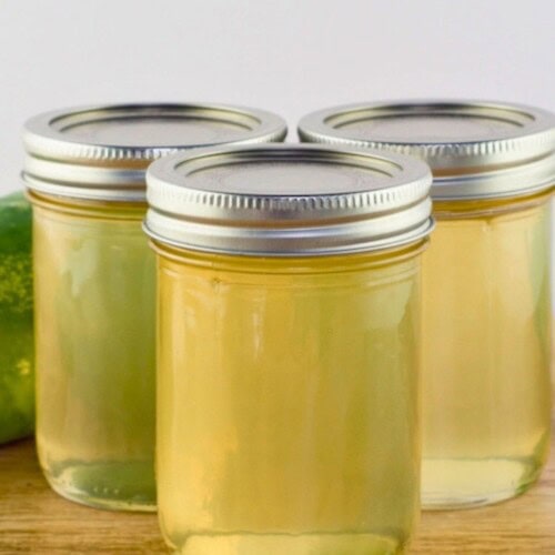 Homemade cucumber jelly in jars on the counter next to a cucumber.