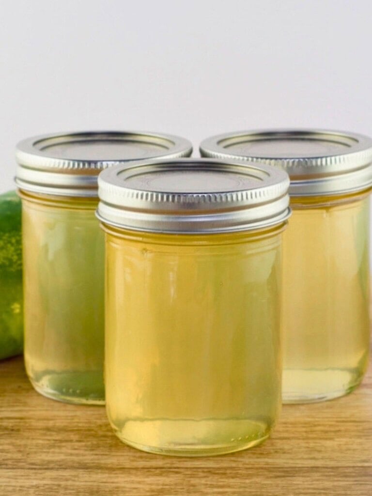 Homemade cucumber jelly in jars on the counter next to a cucumber.