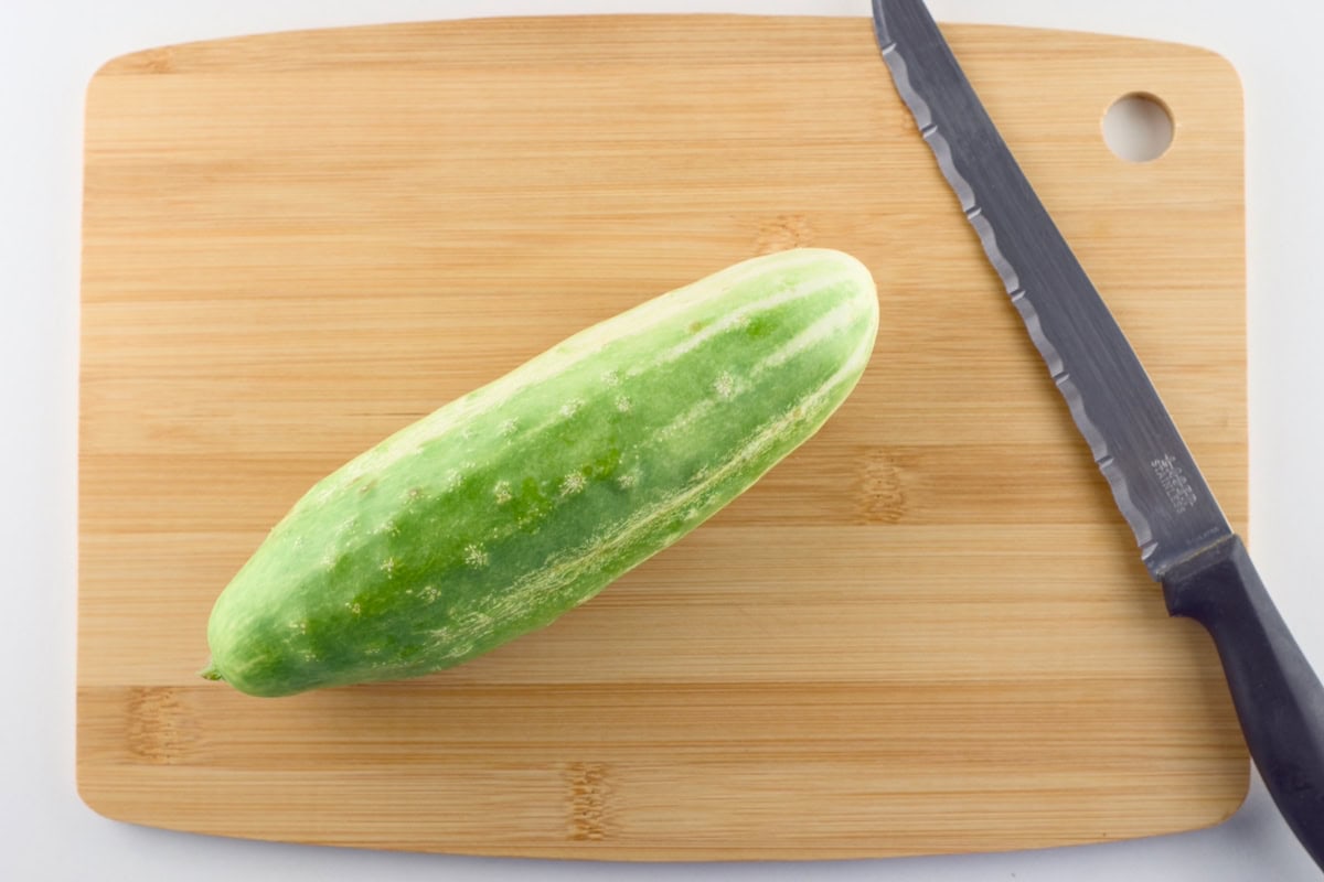 A fresh cucumber and a knife lying on a cutting board.