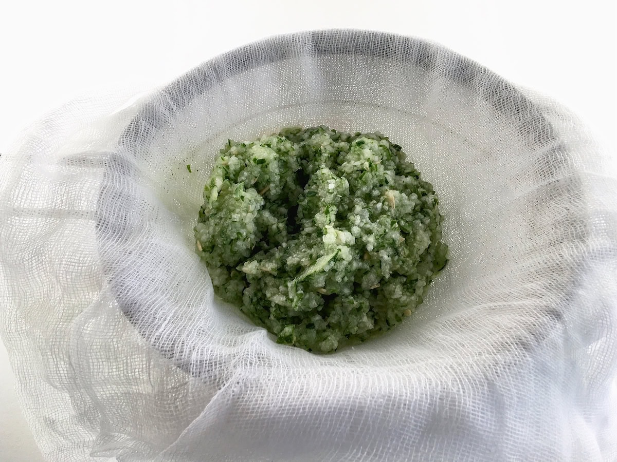 Pureed cucumber pulp draining in a cheesecloth-lined sieve.
