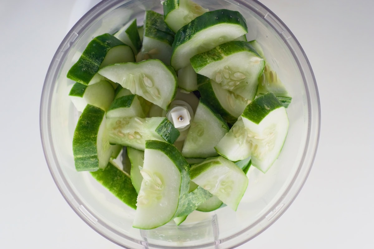 Sliced cucumbers in a food processor bowl.